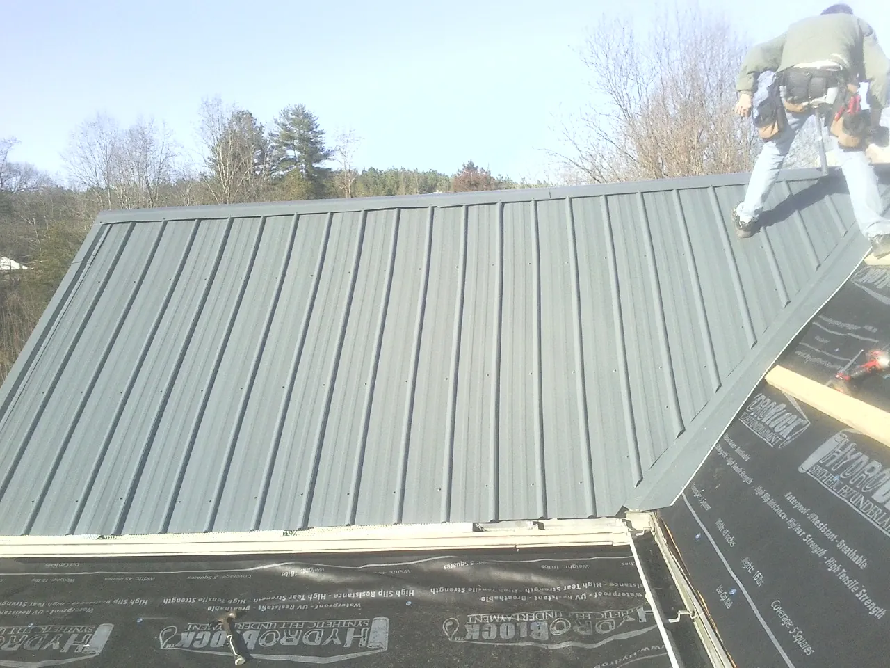 Crew installing dark green standing seam panels over synthetic underlayment in Uvalde