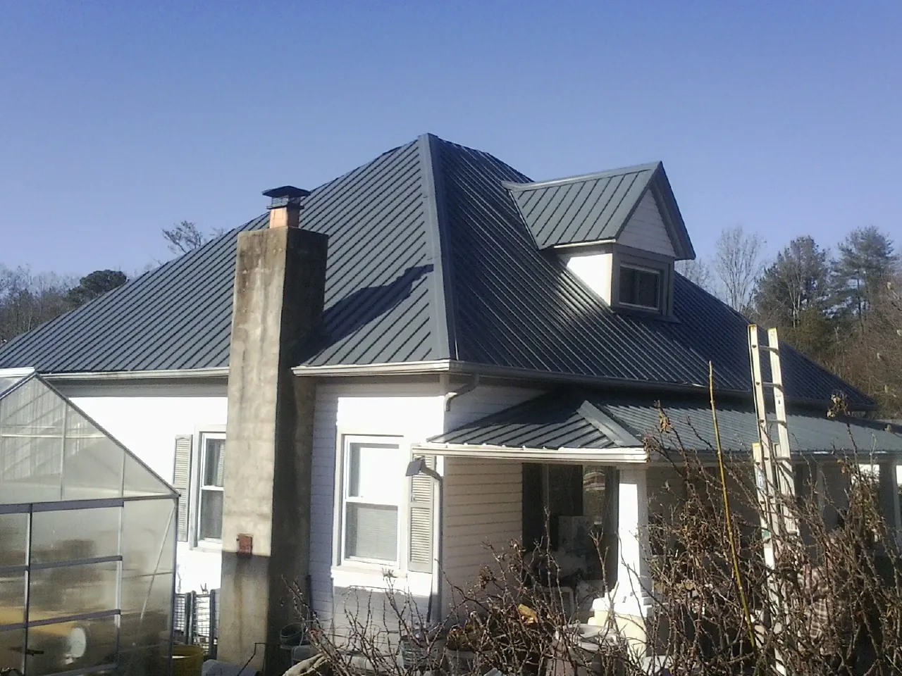 Dark blue standing seam metal roof on a white farmhouse with dormer — Slate & Tile Roof Repair by Roofing Brothers in Uvalde