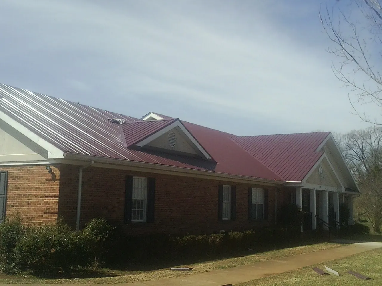 Red metal roof with gabled entries on a long brick building, from a Hail Damage Roof Repair job in Uvalde