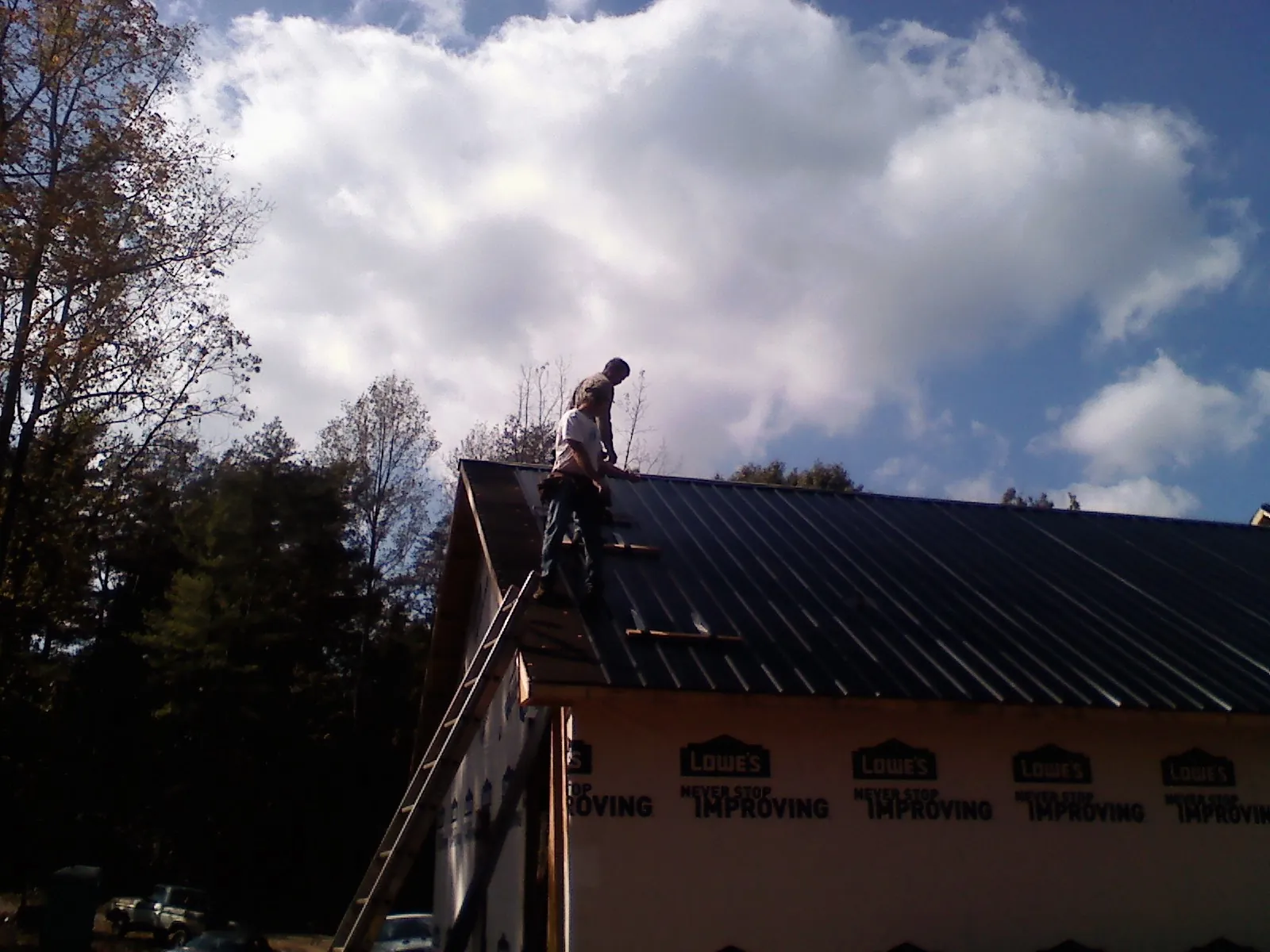 Roofer fastening dark metal panels high against a cloudy sky, from a Roof Inspection job in Uvalde